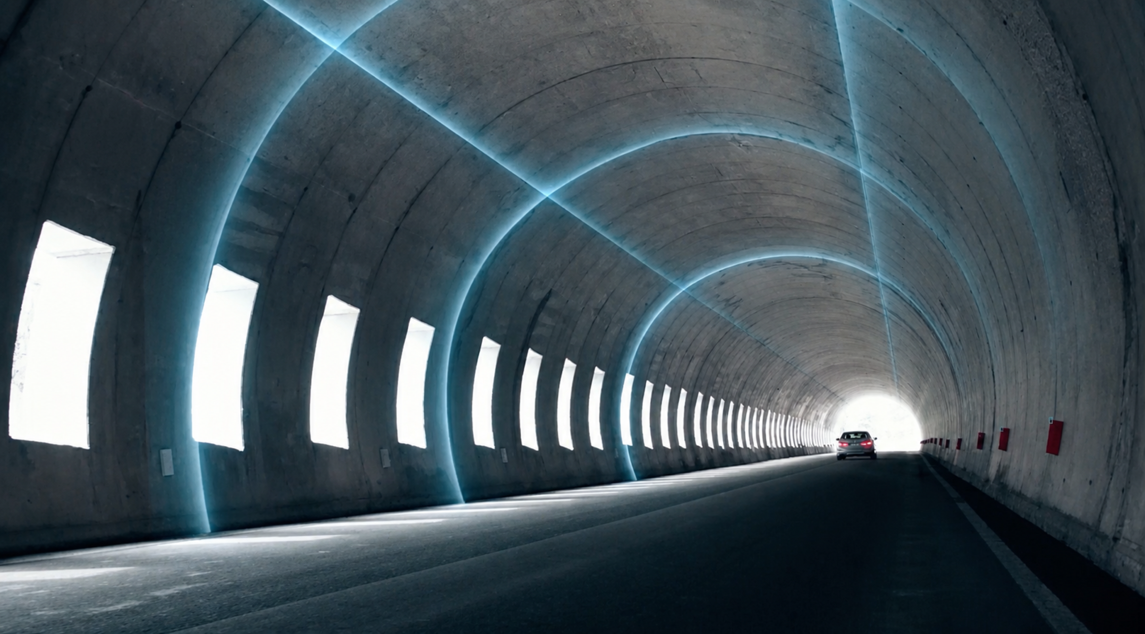 BMW vehicle driving toward daylight through an illuminated concrete tunnel
